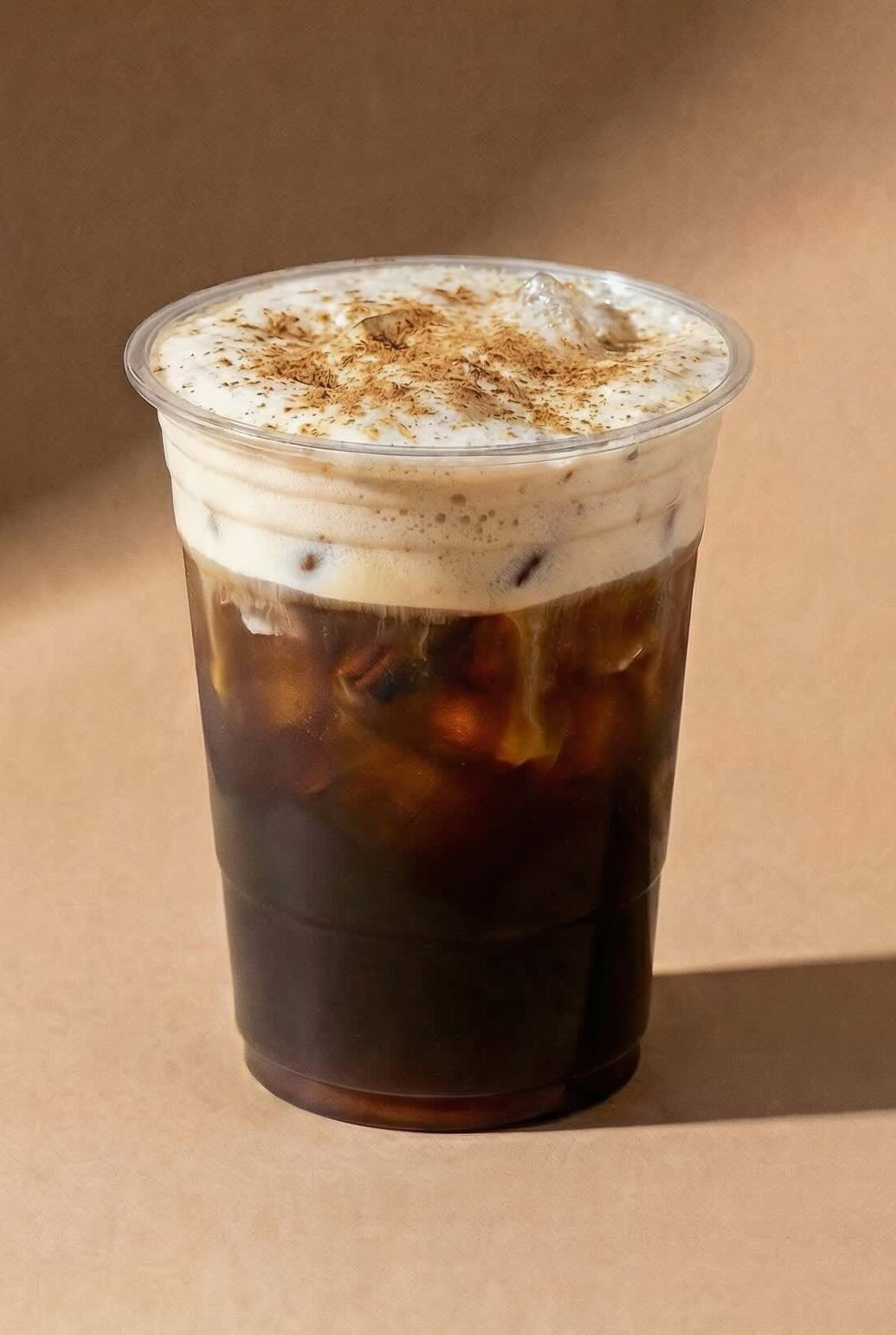 Clear plastic cup with iced cold brew coffee and chai whipped cream on a brown background