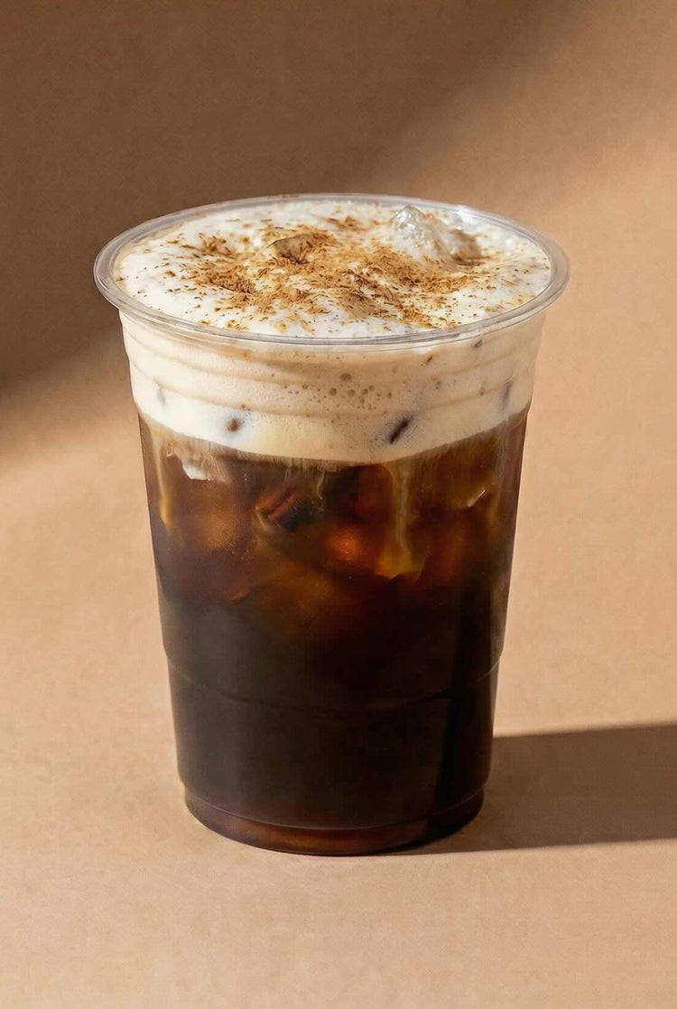 Clear plastic cup with iced cold brew coffee and chai whipped cream on a brown background