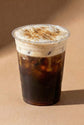 Clear plastic cup with iced cold brew coffee and chai whipped cream on a brown background